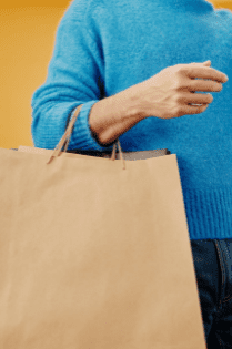 A man in blue sweater holding brown paper bags with one arm.