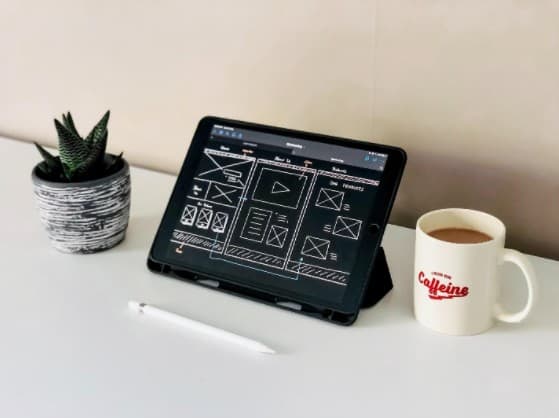 Tablet Displaying Website Wireframe Design with A Coffee on the Table