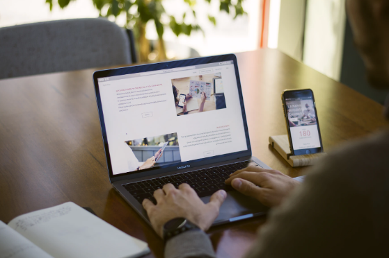 A person on a laptop showing a website beside a mobile phone that displays a similar website