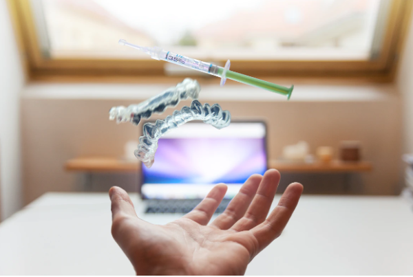 A hand throwing a pair of dentures and syringe upwards in front of a laptop