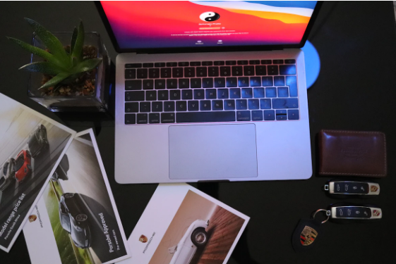 A laptop surrounded by car keys and car pictures