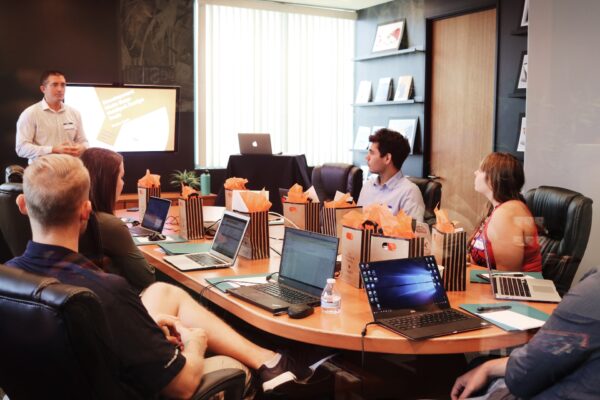 A male instructor training a group of people with laptops in front of them