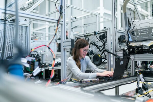 A woman typing on a laptop surrounded by industrial components