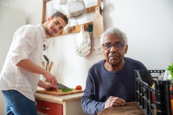 A young, male volunteer assisting an elder man with cooking in the kitchen