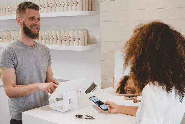 A male staff at the cash register interacting with a lady holding a smartphone