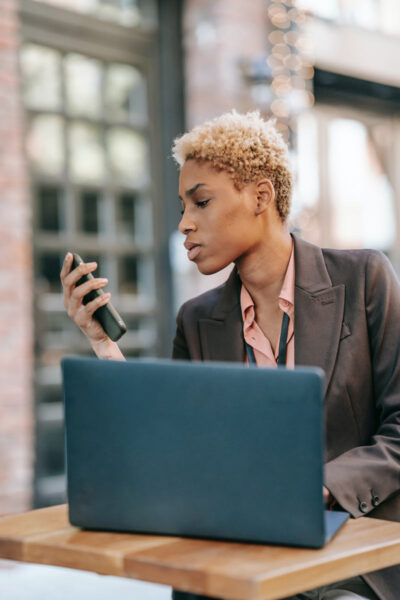 A black female entrepreneur looking at her smartphone while sitting in front of a laptop