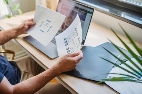 A person holding papers with a laptop and documents on the table.