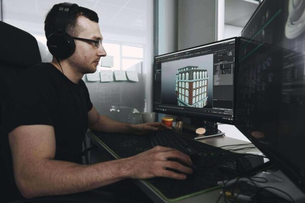 A man in black shirt, eyeglasses and headphones using a computer.